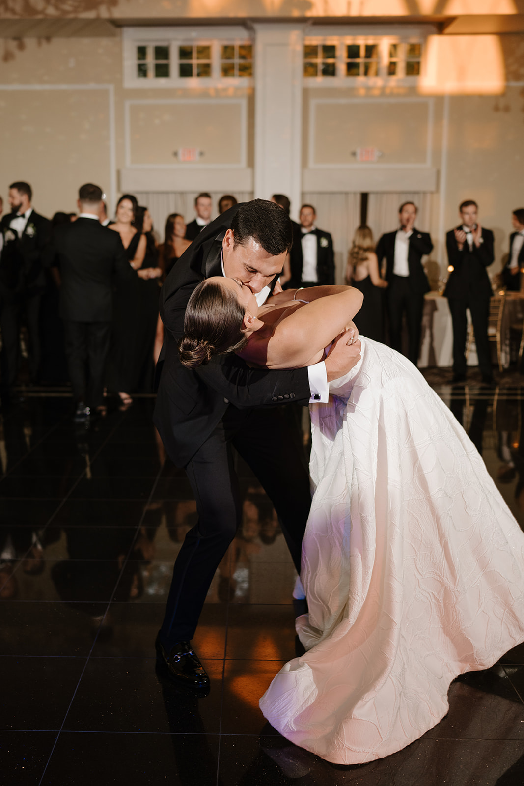 Groom dipping and kissing the bride during their first dance on a reflective black dance floor.